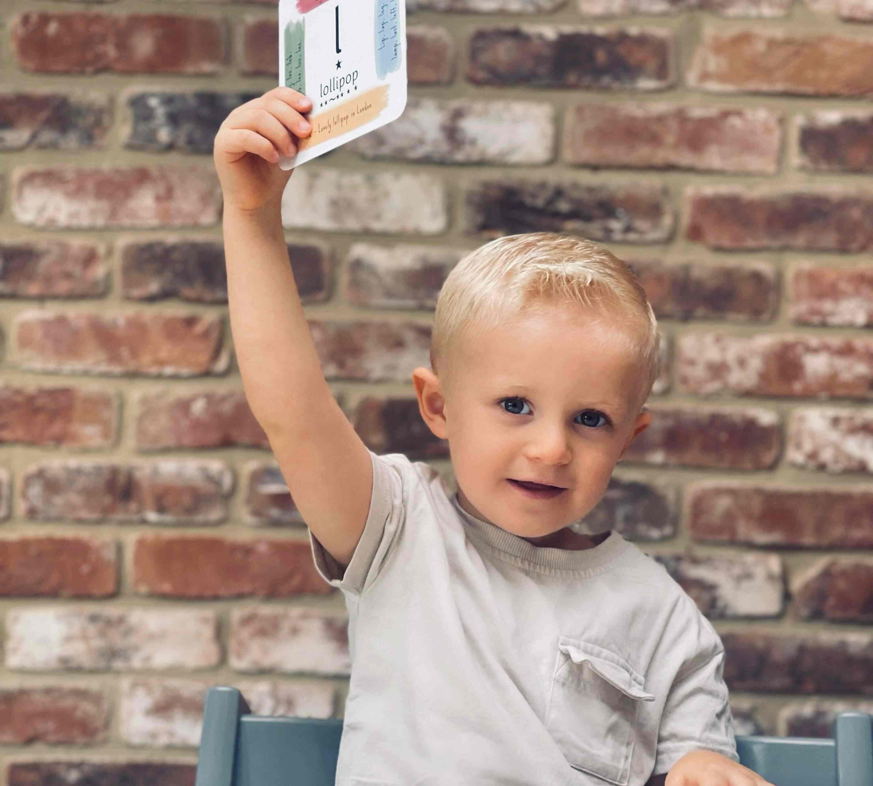 Young boy holding up his phonics cards, smiling.