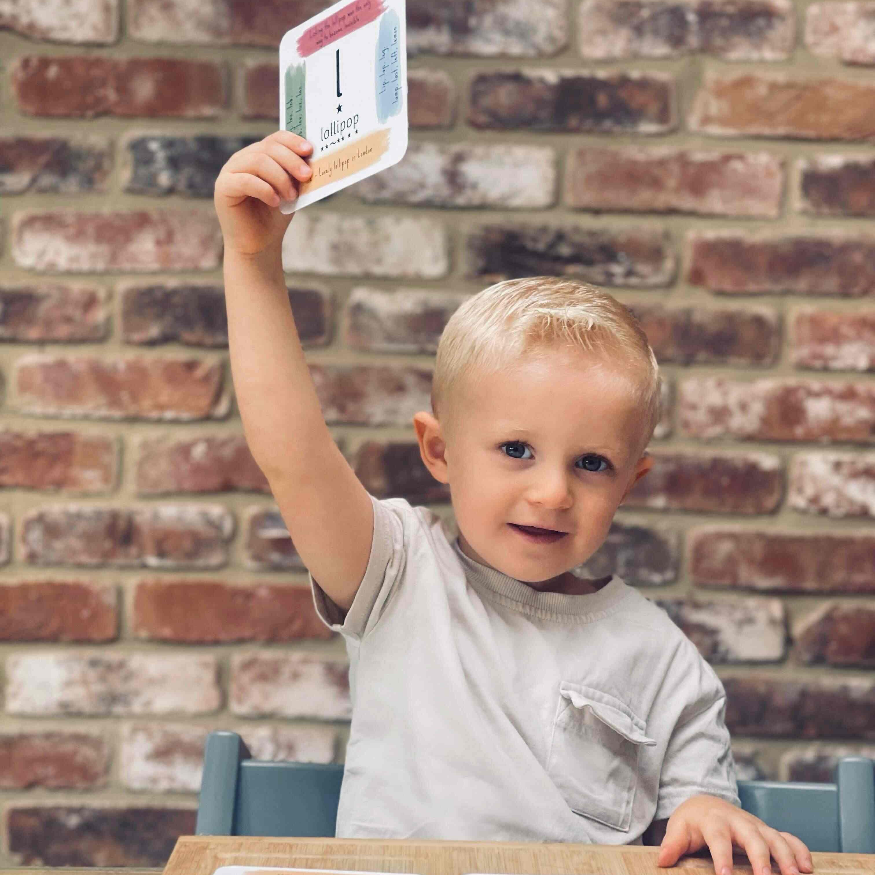 Young boy holding up his phonics cards, smiling.