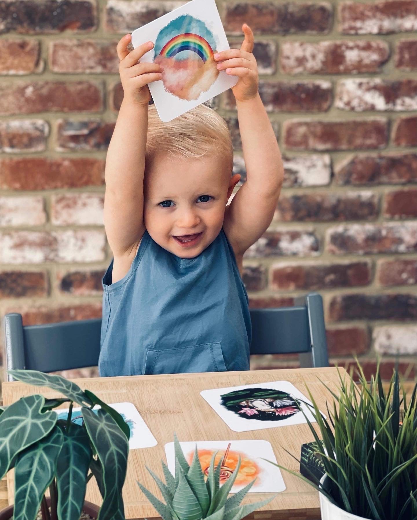 Boy sat at table holding up his rainbow phonics card.
