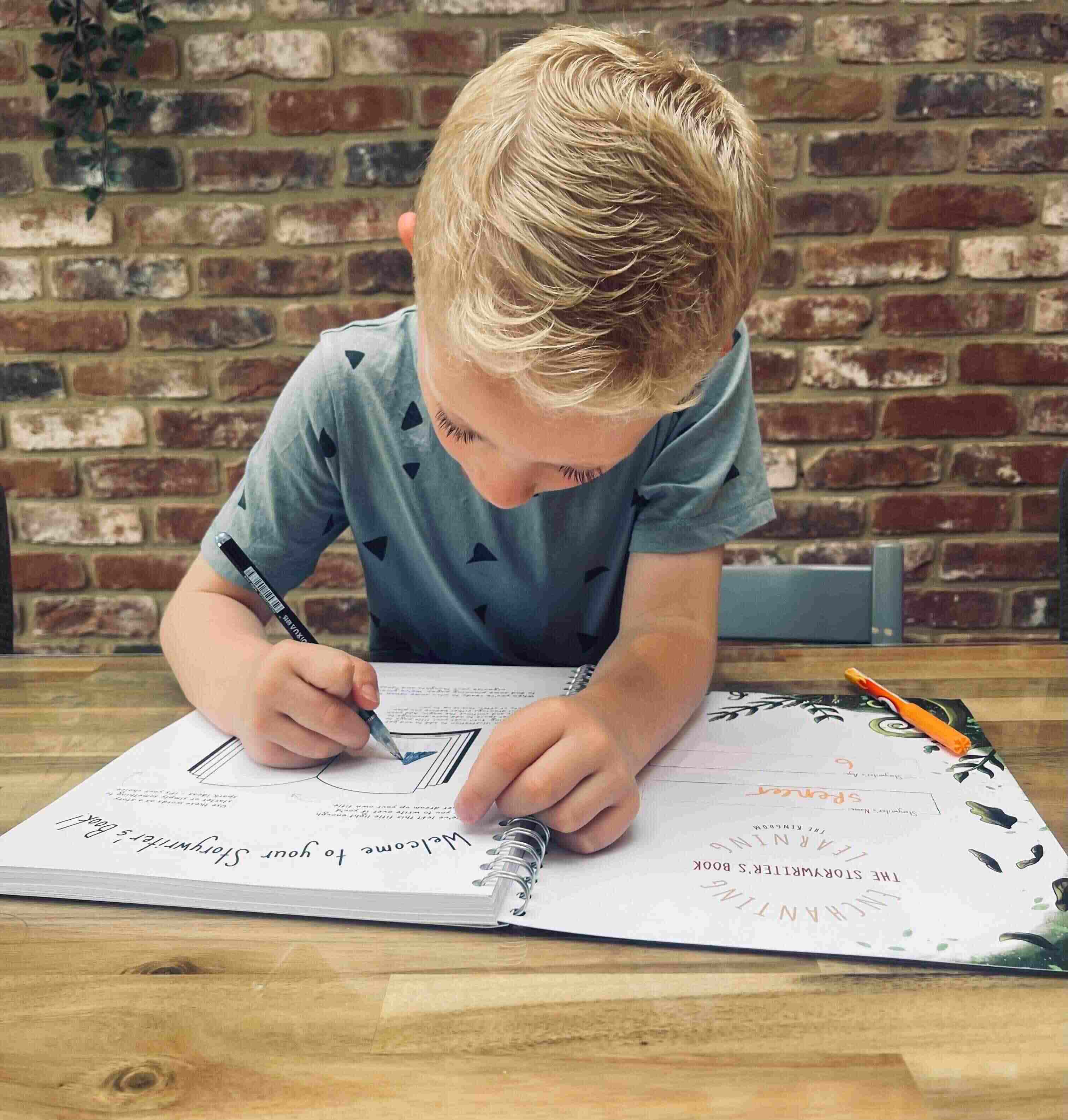 Boy at table writing in his story writing book.