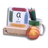 Phonic card showing grapheme card standing in a wooden card stand for phonics cards with an apple and a pot of pencils.
