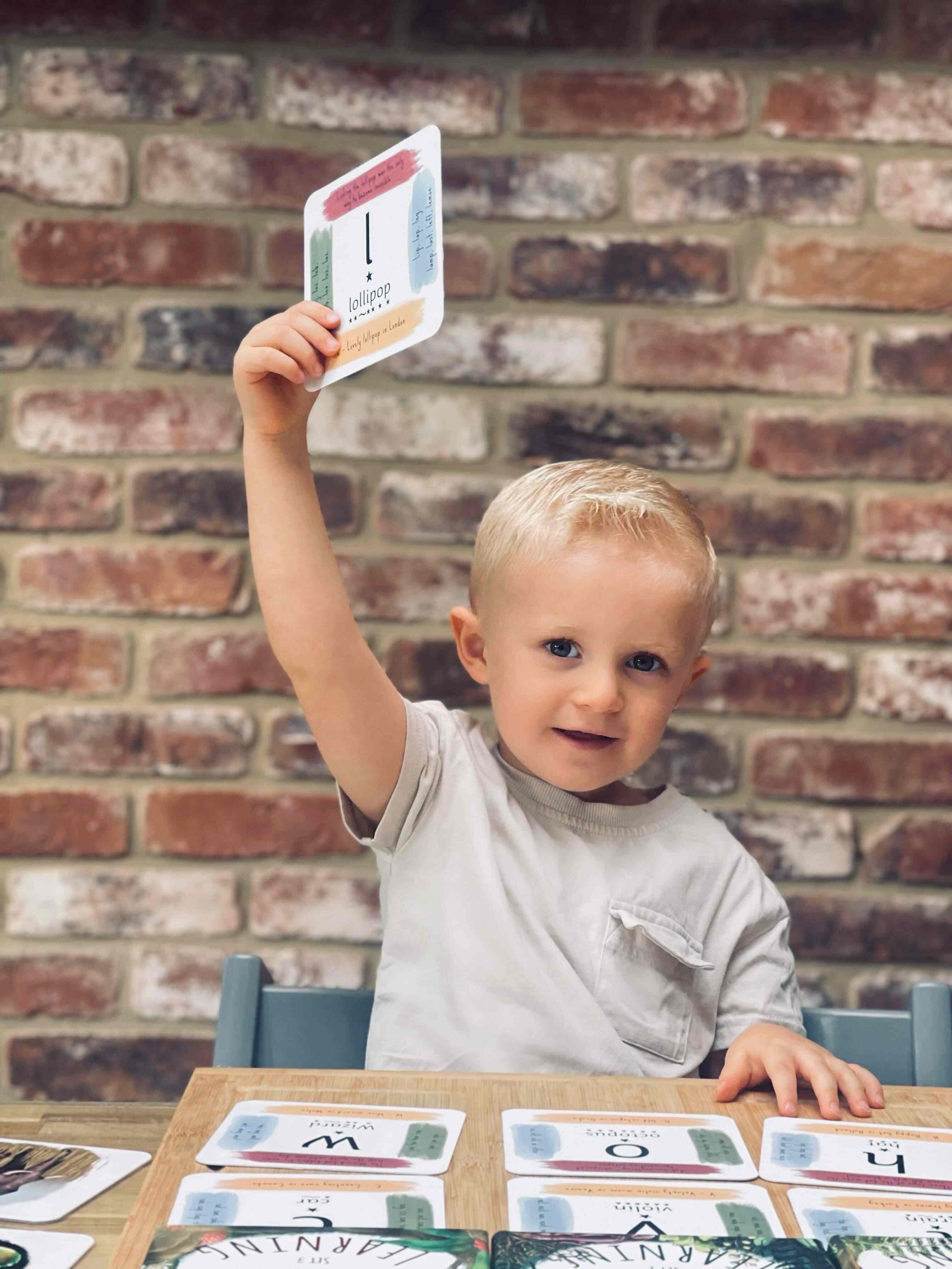 Young boy holding up his phonics cards, smiling.