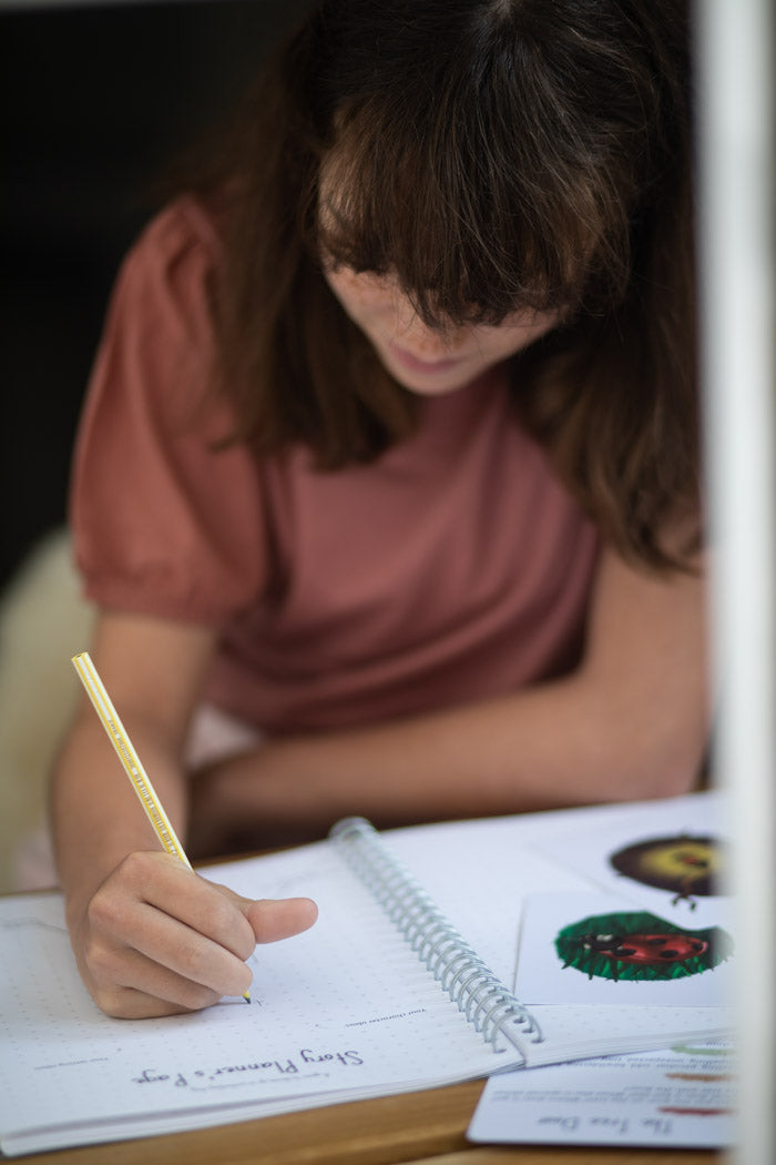 Young girl writing in her book while sat in a window.