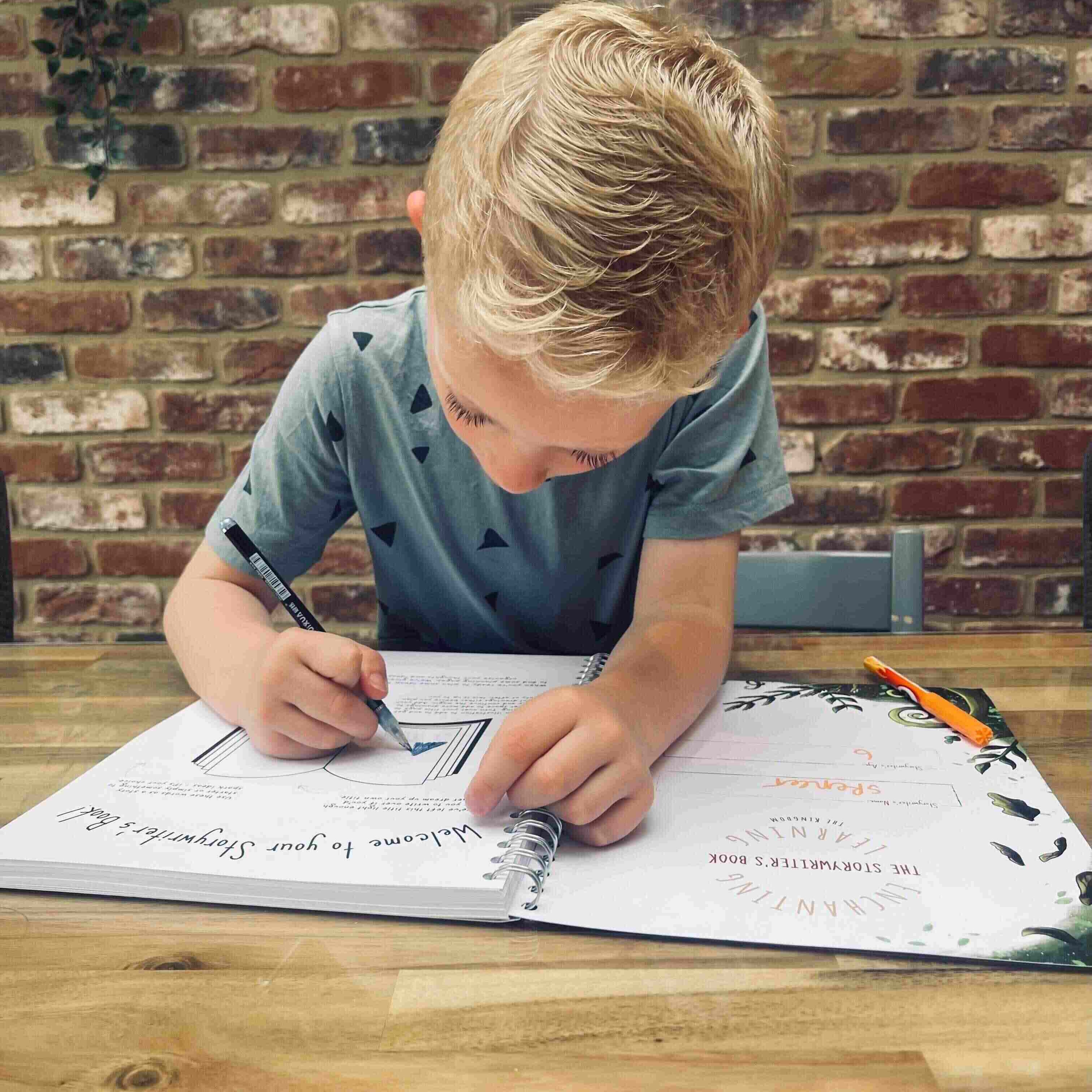 Boy at table writing in his story writing book.