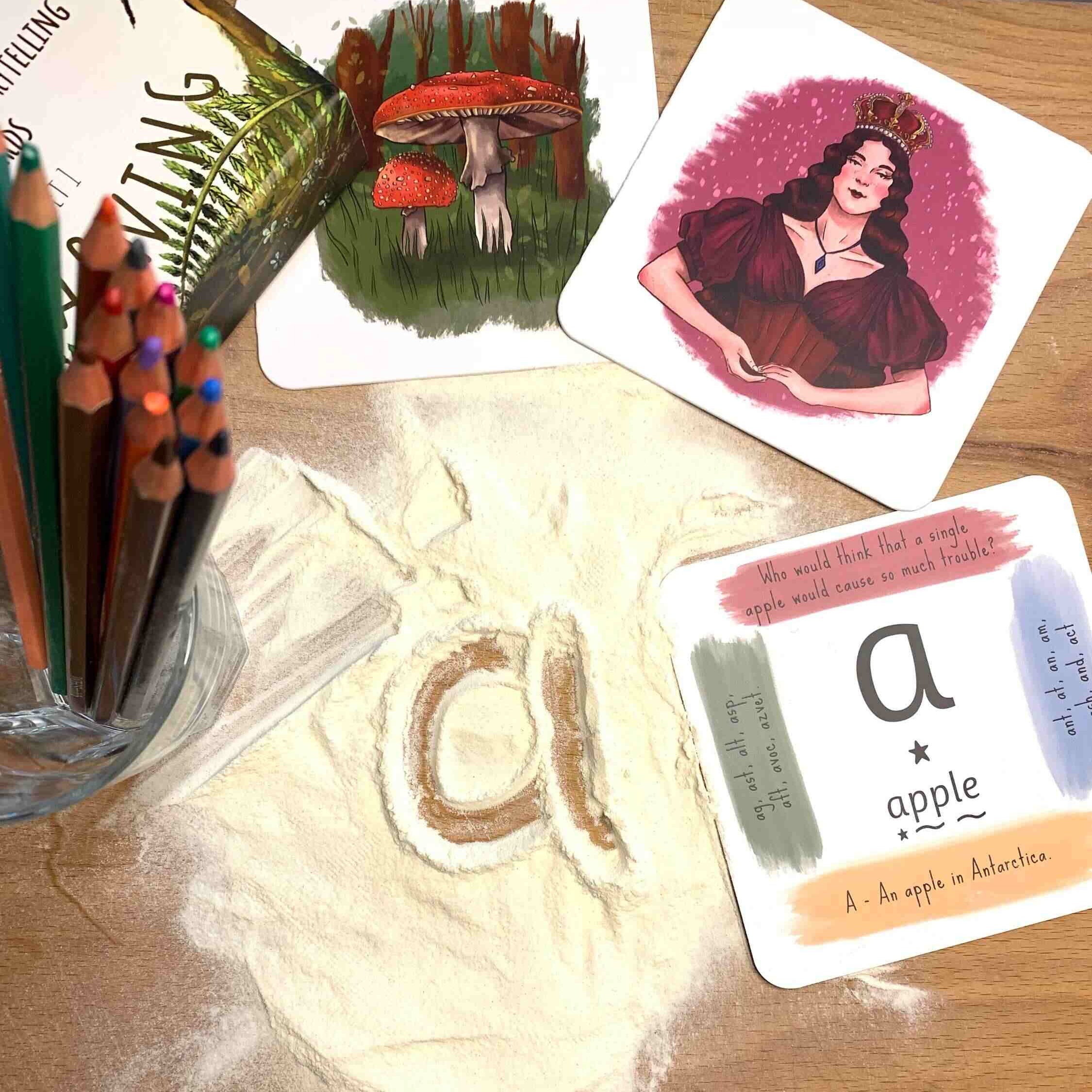 Letters written in flour on work top with queen, mushroom and apple phonics cards.