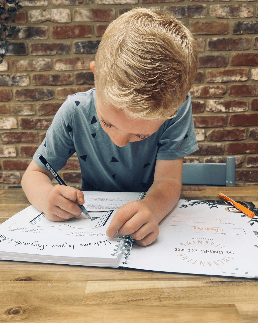 Young boy writing in his story writing book.