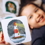 smiling child holding phonics and storytelling card showing a lighthouse illustration.