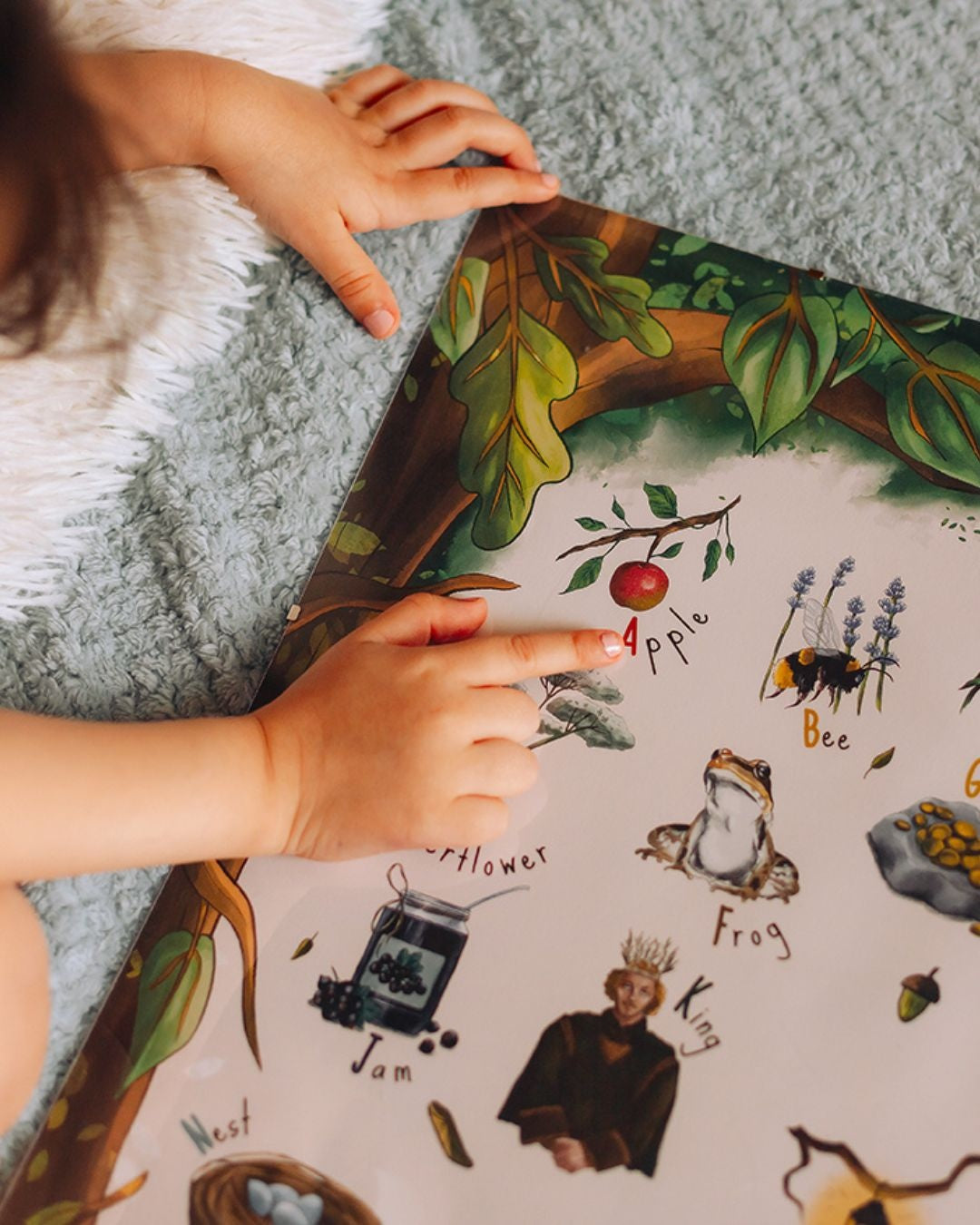 A child's hand pointing to a capital a on a woodland themed poster.