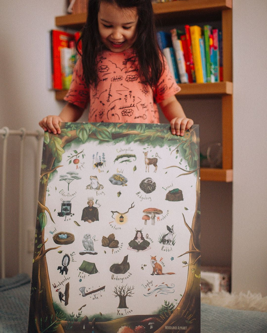 A child holding her woodland alphabet poster, smiling.