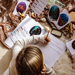Person writing in a notebook with seashells and cards on a textured surface