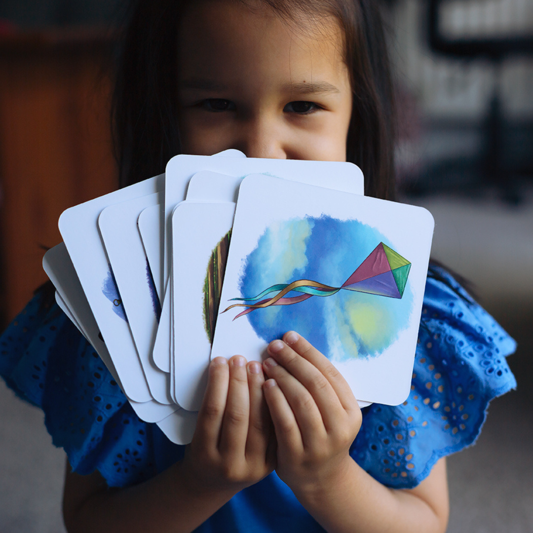 Child holding a deck of cards with colorful designs, including a kite.