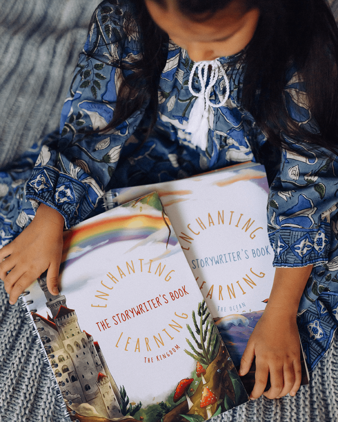 A girl in a blue dress holding two story writing books.