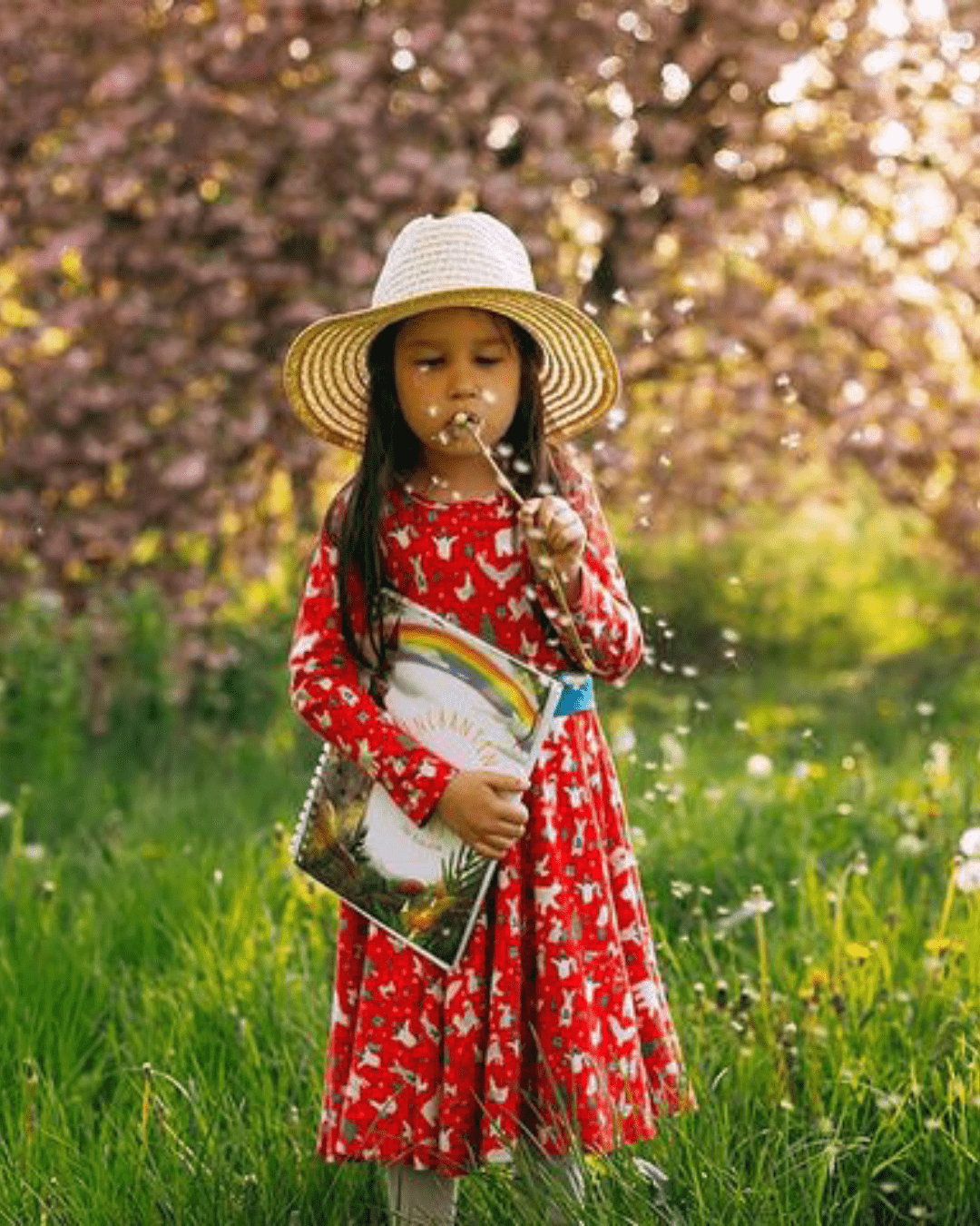 Girl blowing a dandelion in meadow while holding her story writing book.