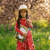 Girl blowing a dandelion in meadow while holding her story writing book.