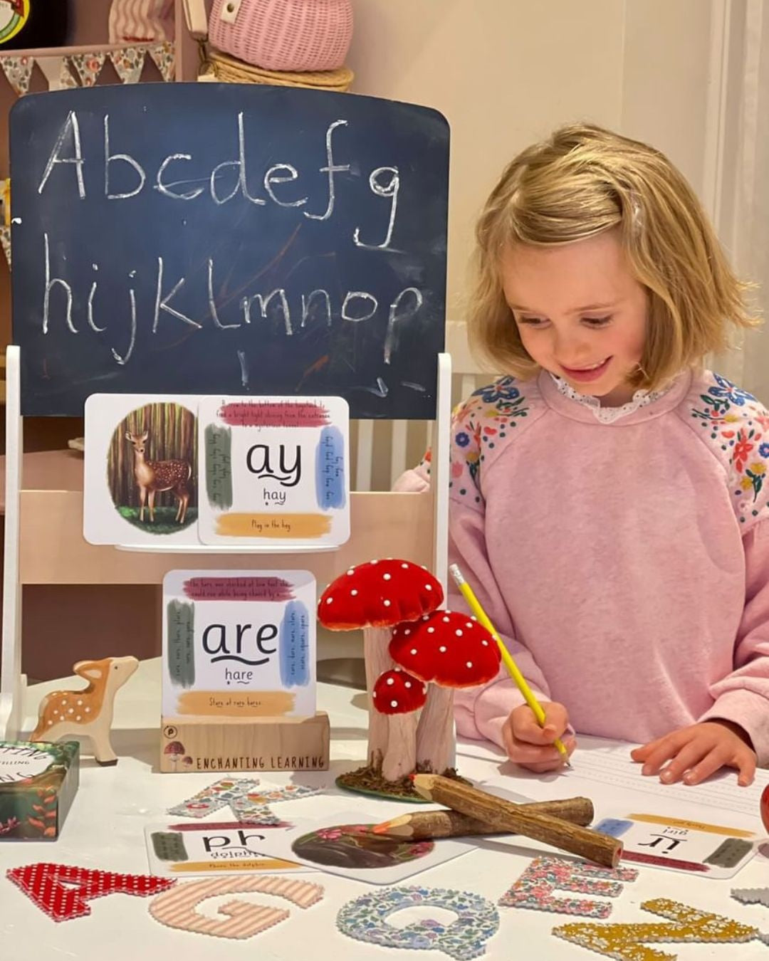 Girl with pencil playing schools with her phonics cards.