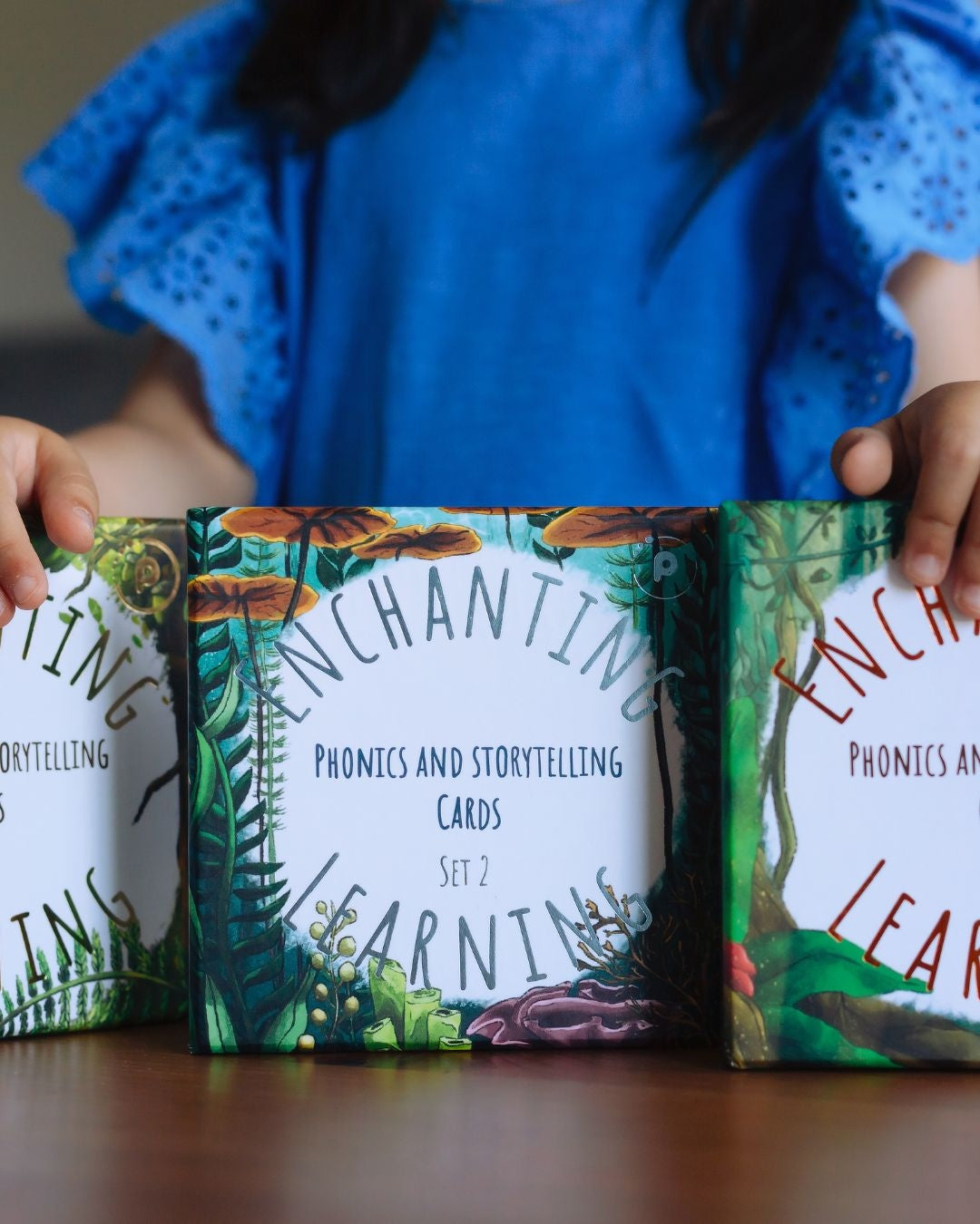 Girl in blue resting hands on three boxes of phonics and storytelling cards.