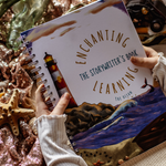 Person holding a notebook titled 'Enchanting The Storyteller's Book Learning The Ocean' surrounded by ocean-themed decor.