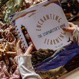 Person holding a notebook titled 'Enchanting The Storyteller's Book Learning The Ocean' surrounded by ocean-themed decor.