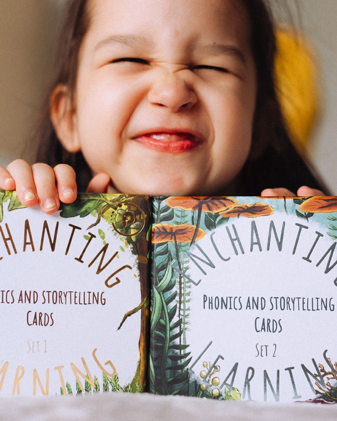 Smiling girl holding two sets of phonics and storytelling cards.