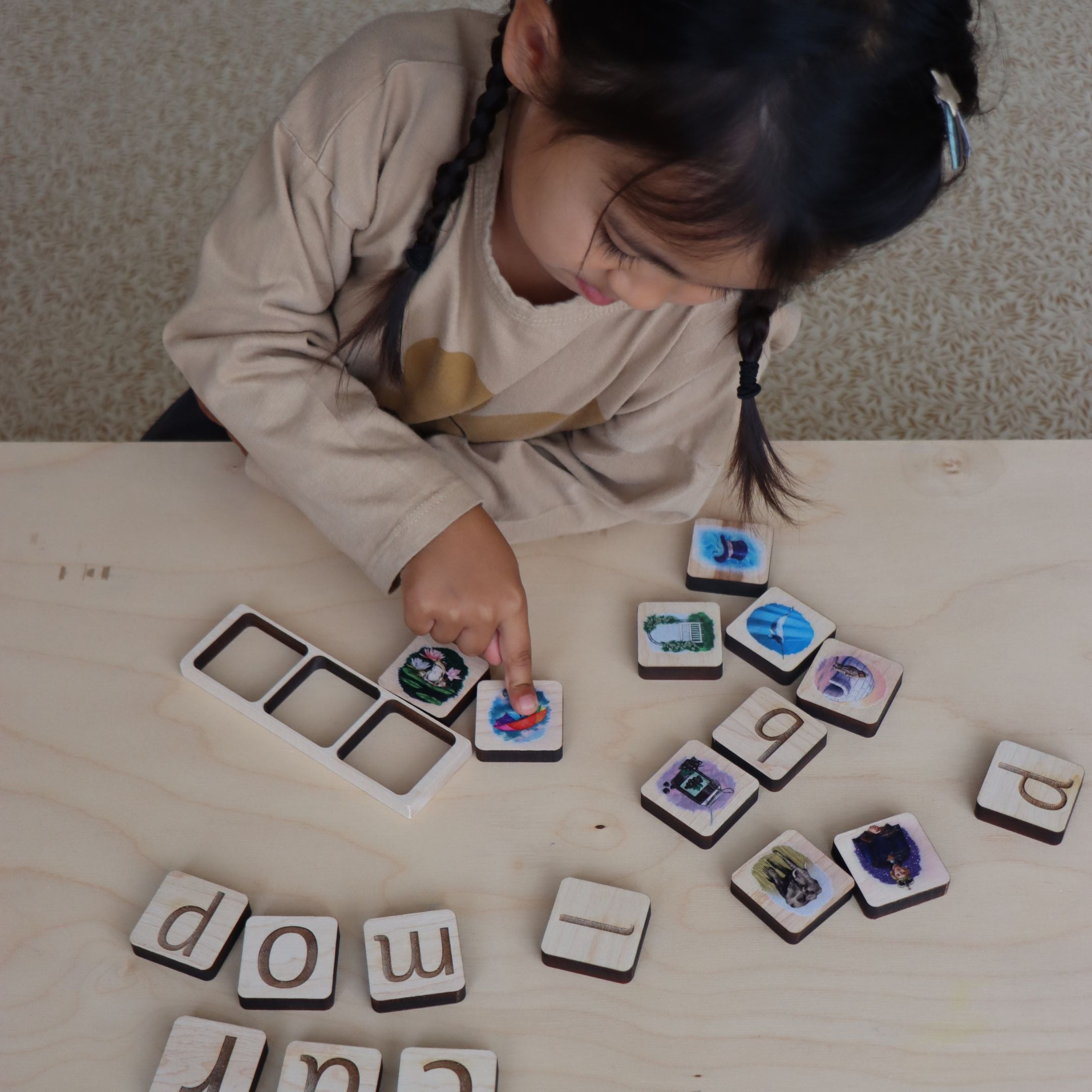 child in pale clothing playing at a wooden table with wooden phonic tiles.