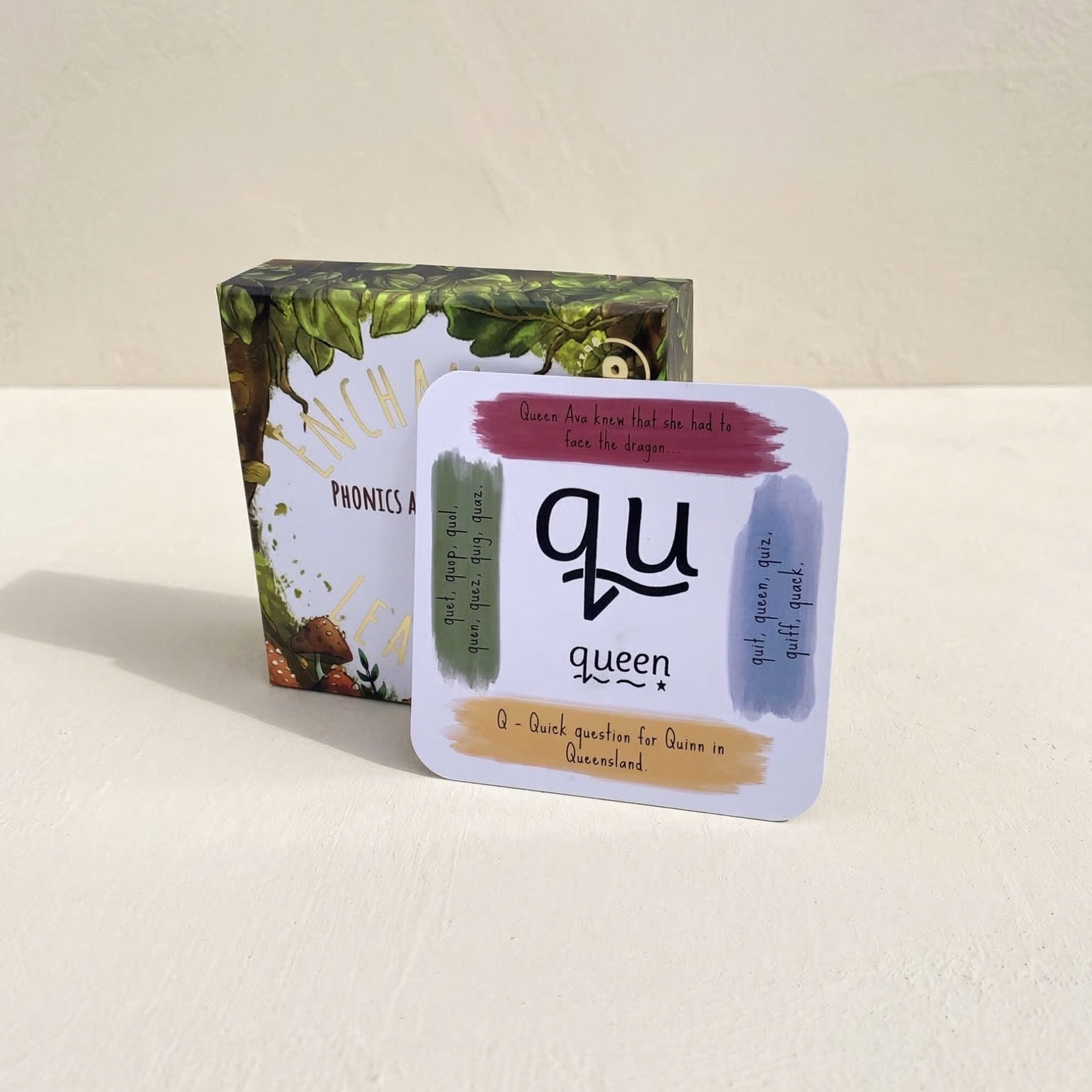 Card with 'qu' and 'queen' text and a box of phonics cards on a beige background