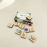 Wooden phonic tiles with letters and a box labeled 'Phonic Tiles' on a light surface.