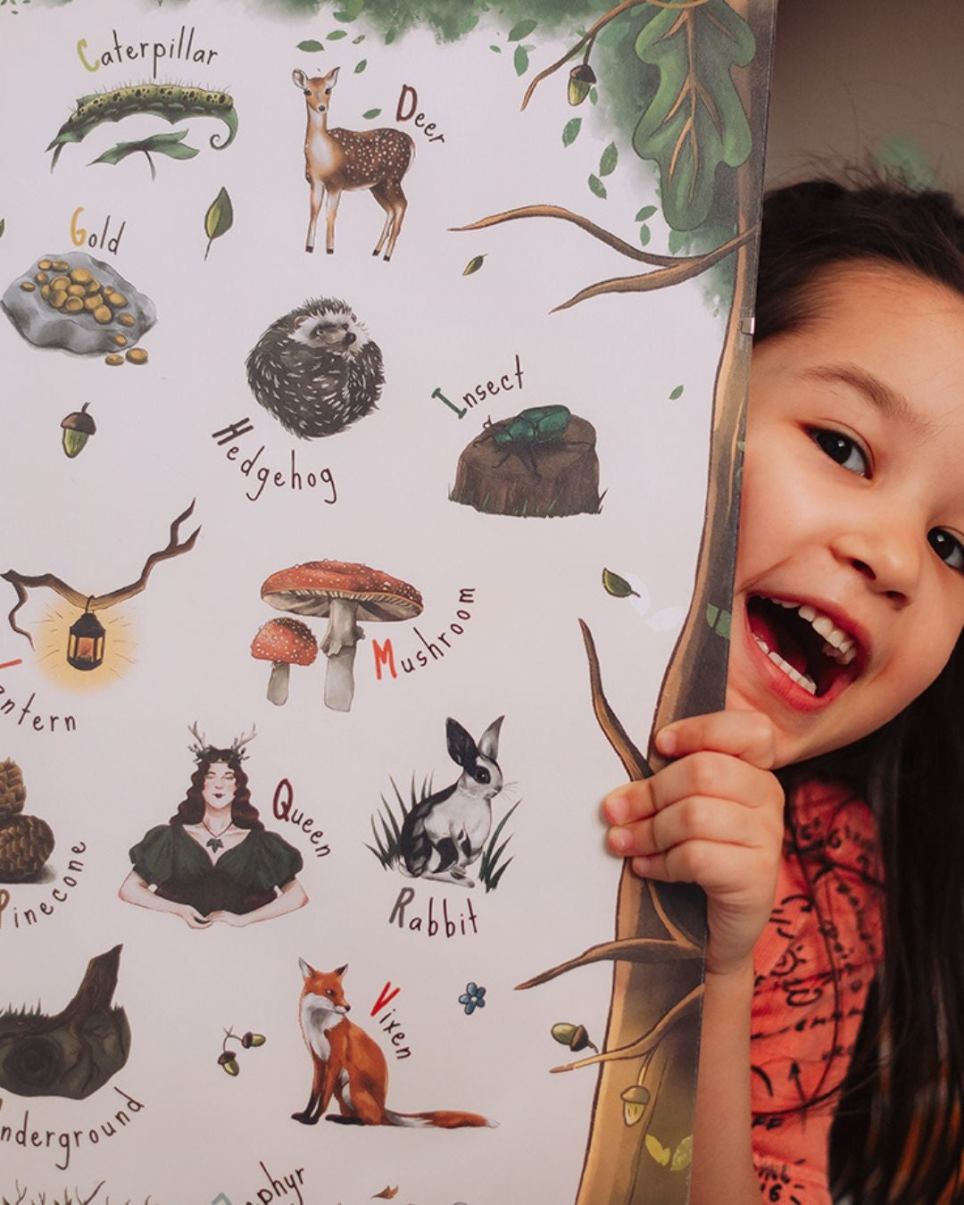 A child holding her woodland alphabet poster, smiling.