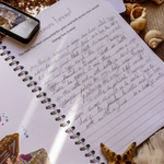 Open writing book with handwritten text, surrounded by decorative items on a textured surface.